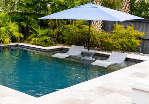 Blue patio umbrella shading lounge chairs on a pool tanning ledge