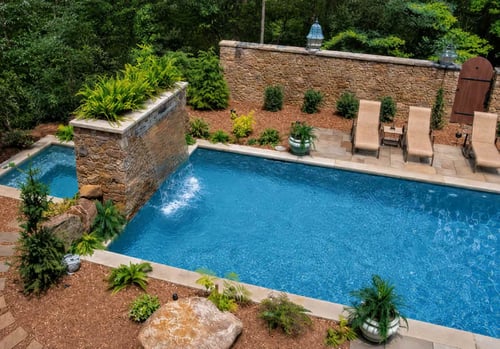 Deep blue pebble pool finish with stone waterfall wall and landscaped backyard