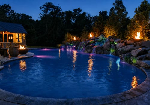 LED pool lighting at night with rock waterfall and fire bowls