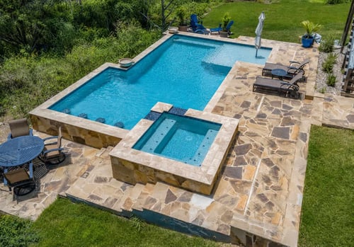 Aerial view of a spacious flagstone pool deck with square spa and outdoor dining