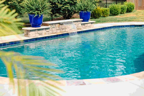 Backyard swimming pool with a sheer descent waterfall feature flanked by cobalt blue ceramic planters