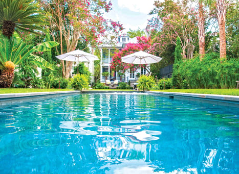 Backyard oasis with gunite swimming pool, vibrant garden, and shaded lounge area behind residential home