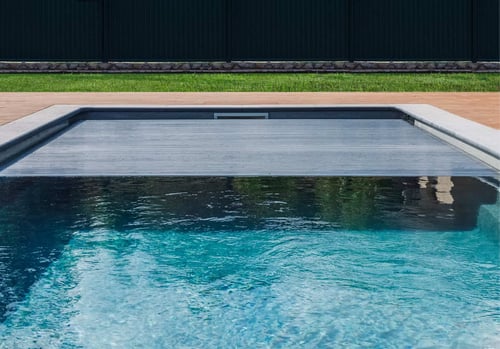 Slatted automatic pool cover retracting to open a clear blue pool