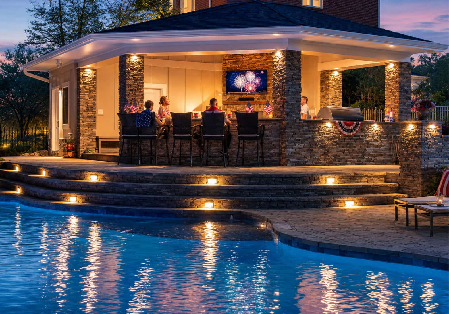 Blue Haven Pools and Spas backyard pool at dusk with outdoor kitchen and family celebrating the 4th of July