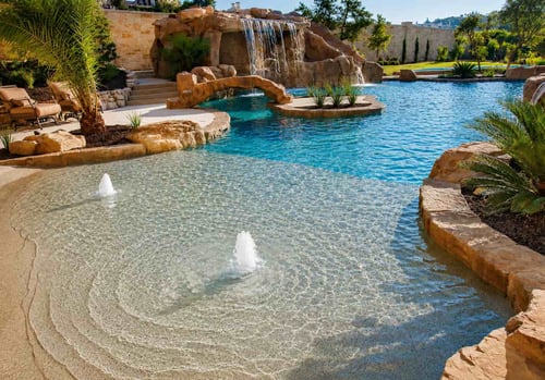 Bubbler fountains on a zero-entry beach pool with tropical landscaping and rock waterfall grotto