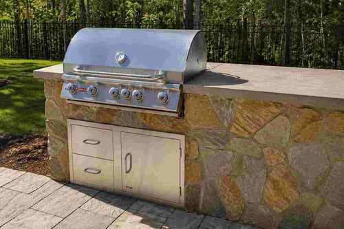 Stainless steel built-in gas grill set into a flagstone outdoor kitchen island with concrete countertop.
