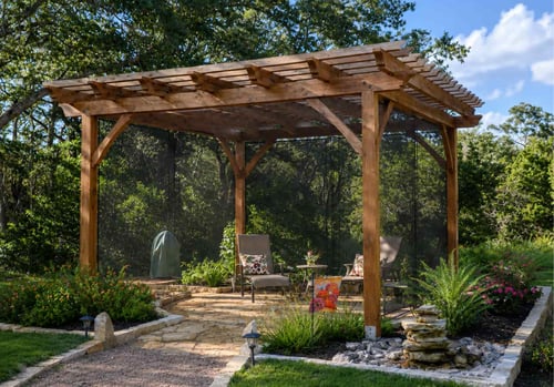 A stained cedar pergola with drop screen curtains enclosing a flagstone patio seating area, surrounded by colorful garden beds, stacked stone accents, and mature oak trees