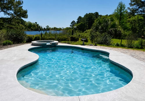 Curved inground pool with integrated spa and concrete deck overlooking landscaped property
