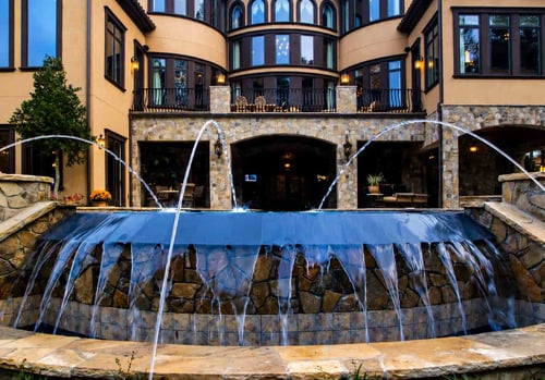 Deck jets and reverse infinity cascade wall on a luxury estate pool at dusk