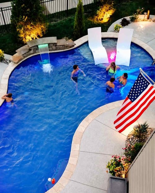 Guests swimming in a backyard pool at a 4th of July party with a large American flag mounted nearby.