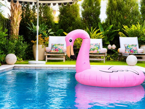 Large pink inflatable flamingo pool float drifting in a landscaped Blue Haven backyard swimming pool.