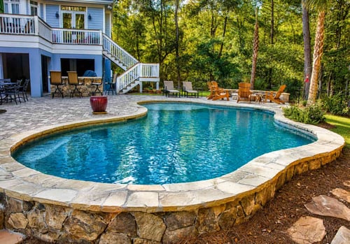 Freeform inground swimming pool with raised stone wall and paver patio in a wooded backyard
