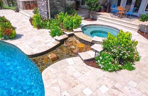 Raised spa spillover flowing into a tropical freeform swimming pool