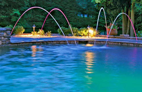 LED-lit laminar water jets arcing into a custom pool at night