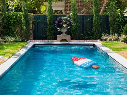 nflatable red, white, and blue ice pop pool float drifting in a landscaped backyard swimming pool