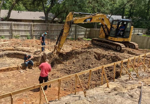 CAT excavator digging inground pool foundation with workers and safety fencing during the construction phase.