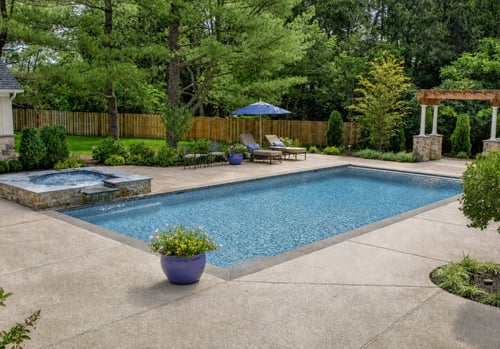 Finished inground pool with attached spa, concrete deck, and lounge seating area in backyard