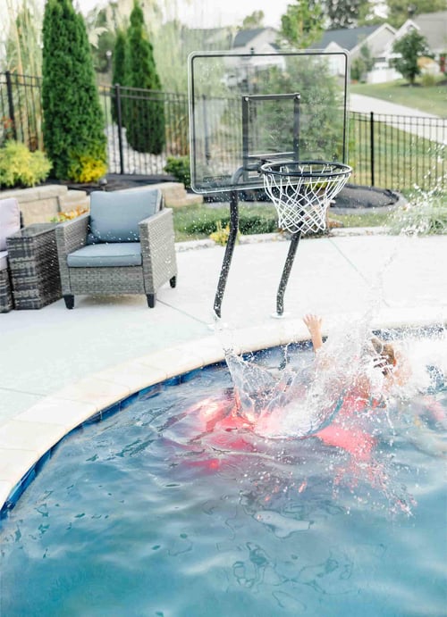 Child splashing into a Blue Haven inground pool next to a poolside basketball hoop