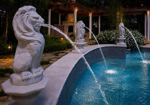 Three lion spouting statues shooting arcing water streams into an elegant curved pool at night