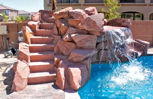 Stone staircase leading to rock waterfall feature spilling into a backyard swimming pool