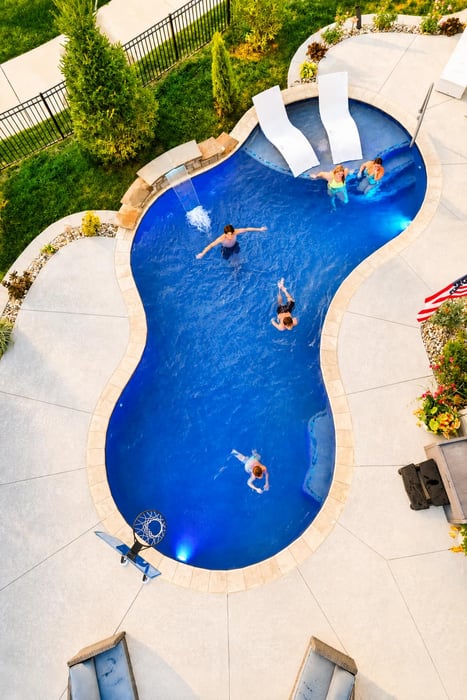 Aerial view of a freeform Blue Haven backyard pool with swimmers, a waterfall, and a poolside basketball hoop.