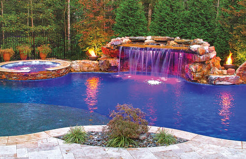 Custom pool with grotto waterfall and LED lighting illuminating cascading water in daytime