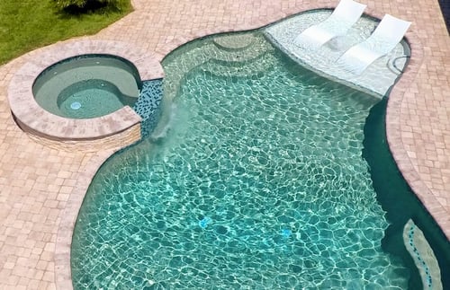 Aerial view of pool sun shelf with white chaise lounge positioned next to an attached spa
