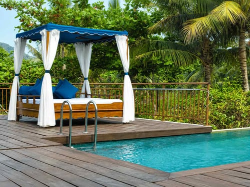 Poolside cabana with blue canopy and white curtains next to an inground pool
