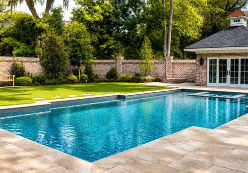 Rectangular inground pool with travertine deck, brick privacy wall, and pool house