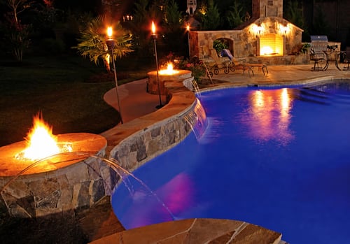 Stone fire pit integrated into curved pool perimeter wall with built-in seating at night