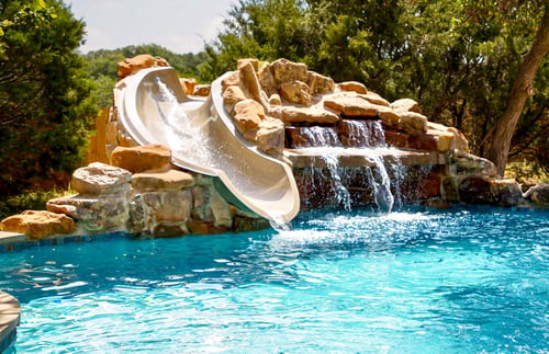 Rock waterfall grotto with dual slides flowing into a clear blue swimming pool