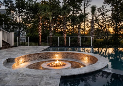 Sunken fire pit with stone seating area beside infinity pool at sunset