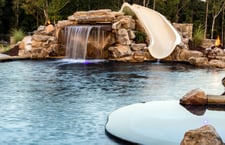 Backyard pool with rock waterfall and single curved slide next to raised spa
