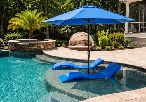 Two blue chaise lounges on a pool sun shelf with patio umbrella in a custom backyard pool