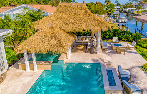 Tropical backyard pool with thatched shade structure and raised spa