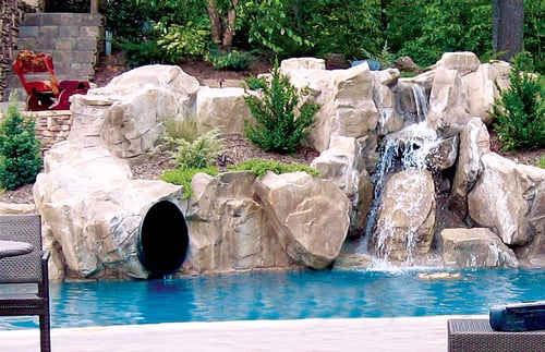 Rock waterfall feature with tunnel-style slide opening into a swimming pool
