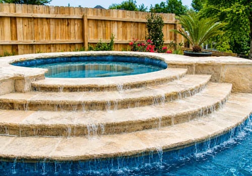 Elevated spa with a weeping spillway cascading water down stepped travertine levels into the pool